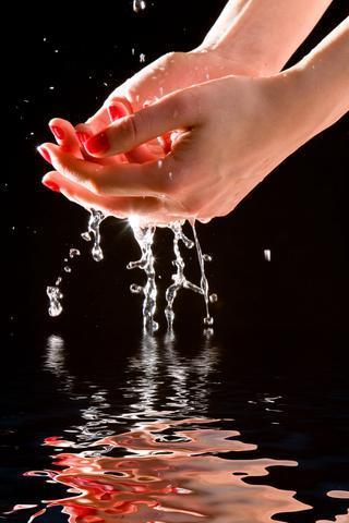 Pair of hands under running water, against a black background and reflected in the water.