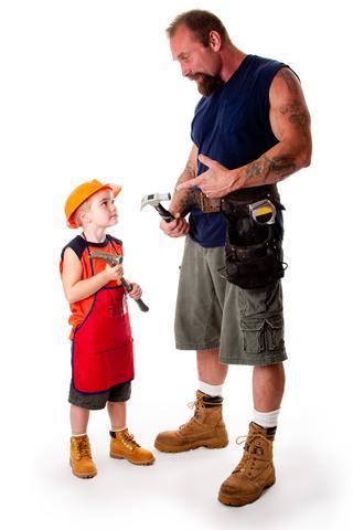 Muscular carpenter, dressed for work and holding a hammer. Beside him his son, similarly dressed for work. Both are holding hammers and the father is instructing his son about the tool.