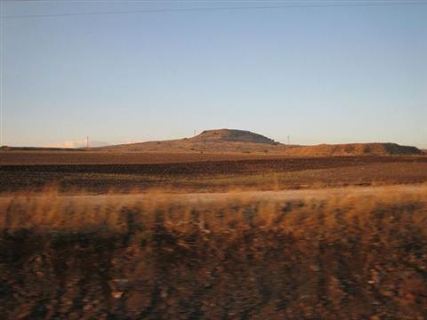 Low peak viewed rising above a plain, a secondary peak rises adjacent but somewhat lower.