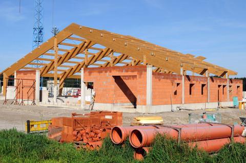 Red-brick barn, part-built and with joists exposed against a vivid blue sky as they wait for the roof