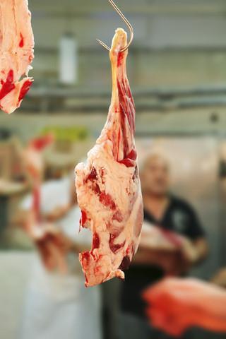 Raw leg of lamb, hanging from a hook in a butcher’s shop